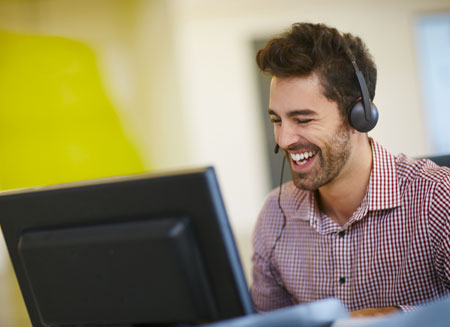 A smiling man wearing a telephone headset uses a computer to create an association shipping program.