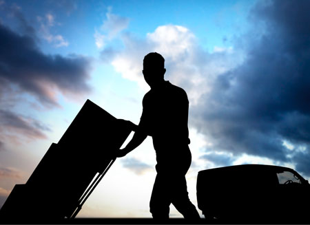 A silhouette of a man delivering several small packages on a dolly.