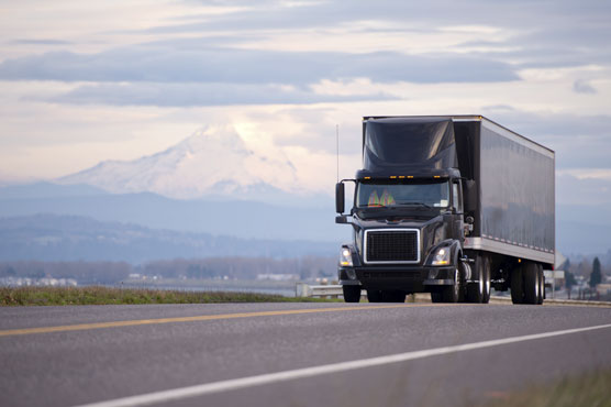 A semi-truck driving down a two-lane highway, shown from the front, with mountains in the background.