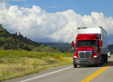 A red semi-truck carrying guaranteed L T L freight drives down a two-lane highway.