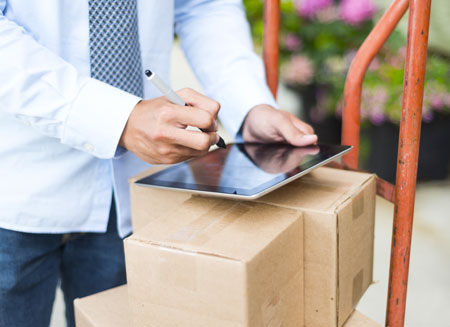 A man uses a computer tablet that is sitting on top of several small shipping boxes. 