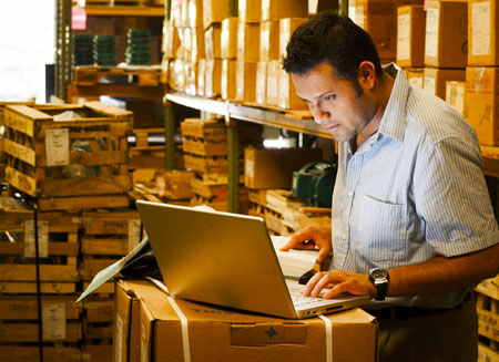 Standing in front of a laptop computer in a warehouse, a man purchases L T L freight insurance.