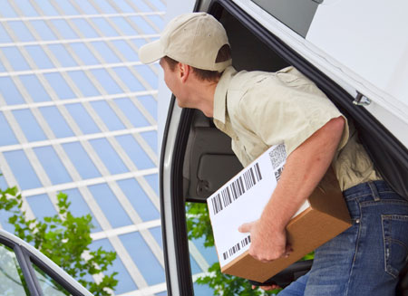 A small package delivery man gets out of his truck with a package under his arm.