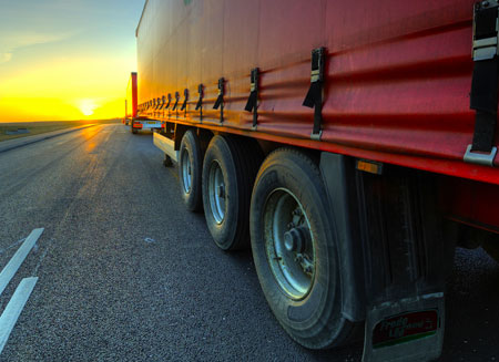A red semi delivering a full truckload of freight is shown from the rear driving into a setting sunA red semi delivering a full truckload of freight is shown from the rear driving into a setting sun.