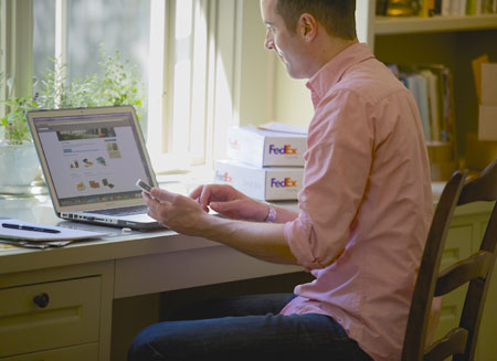 A man is sitting at a desk with several FedEx boxes on it, using a laptop computer.